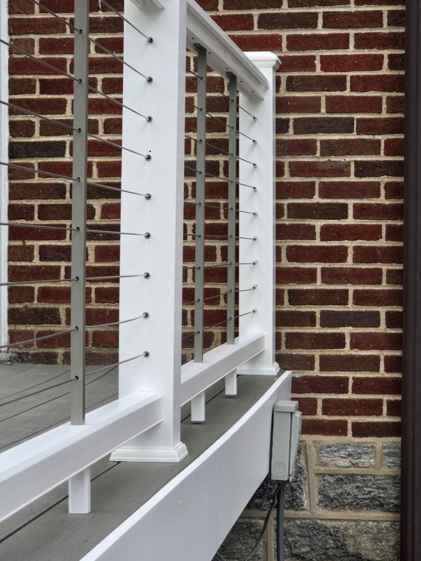 Detail of white cable railing posts against brick wall