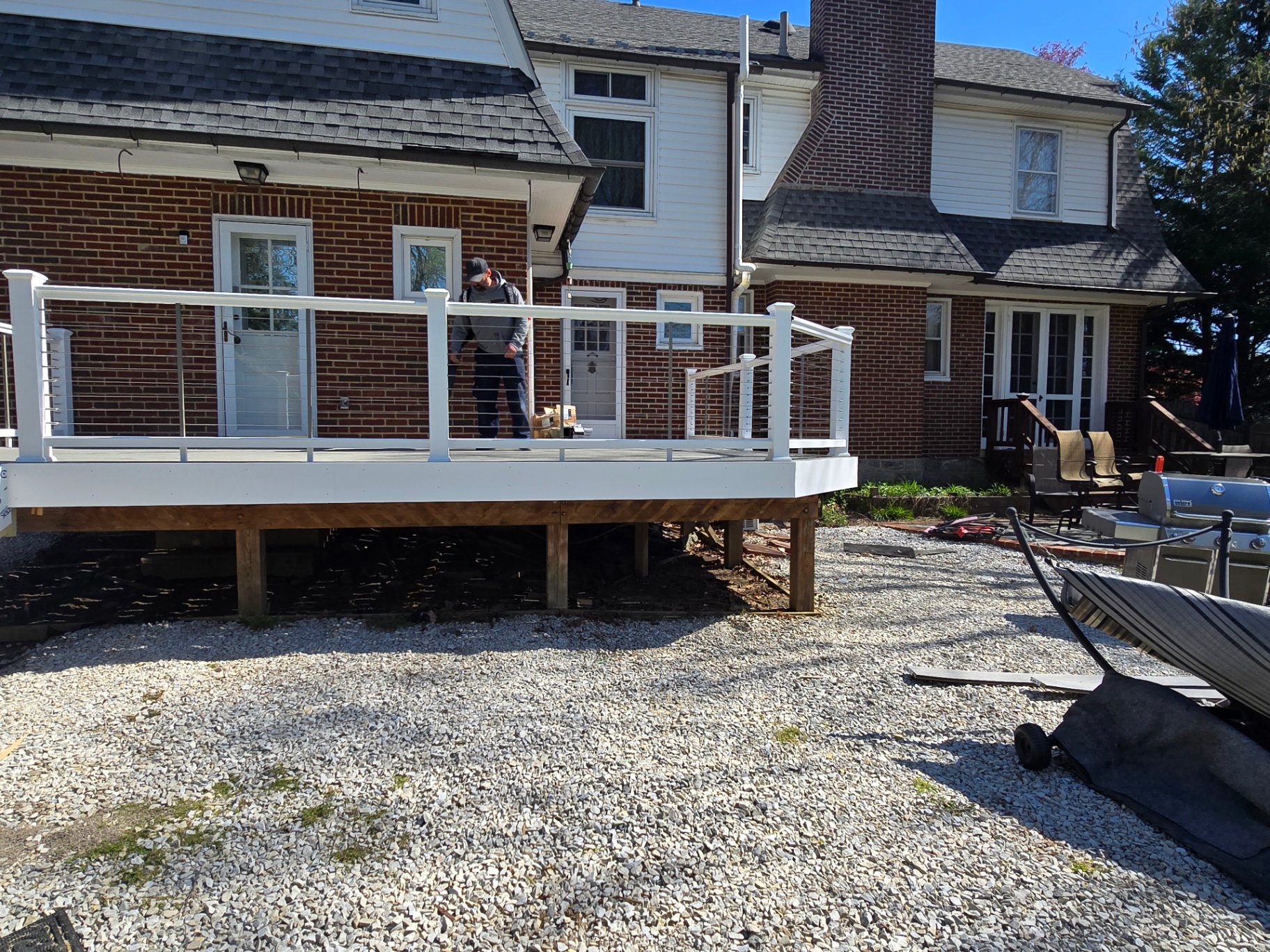 Finished elevated composite deck with white cable railings behind brick home