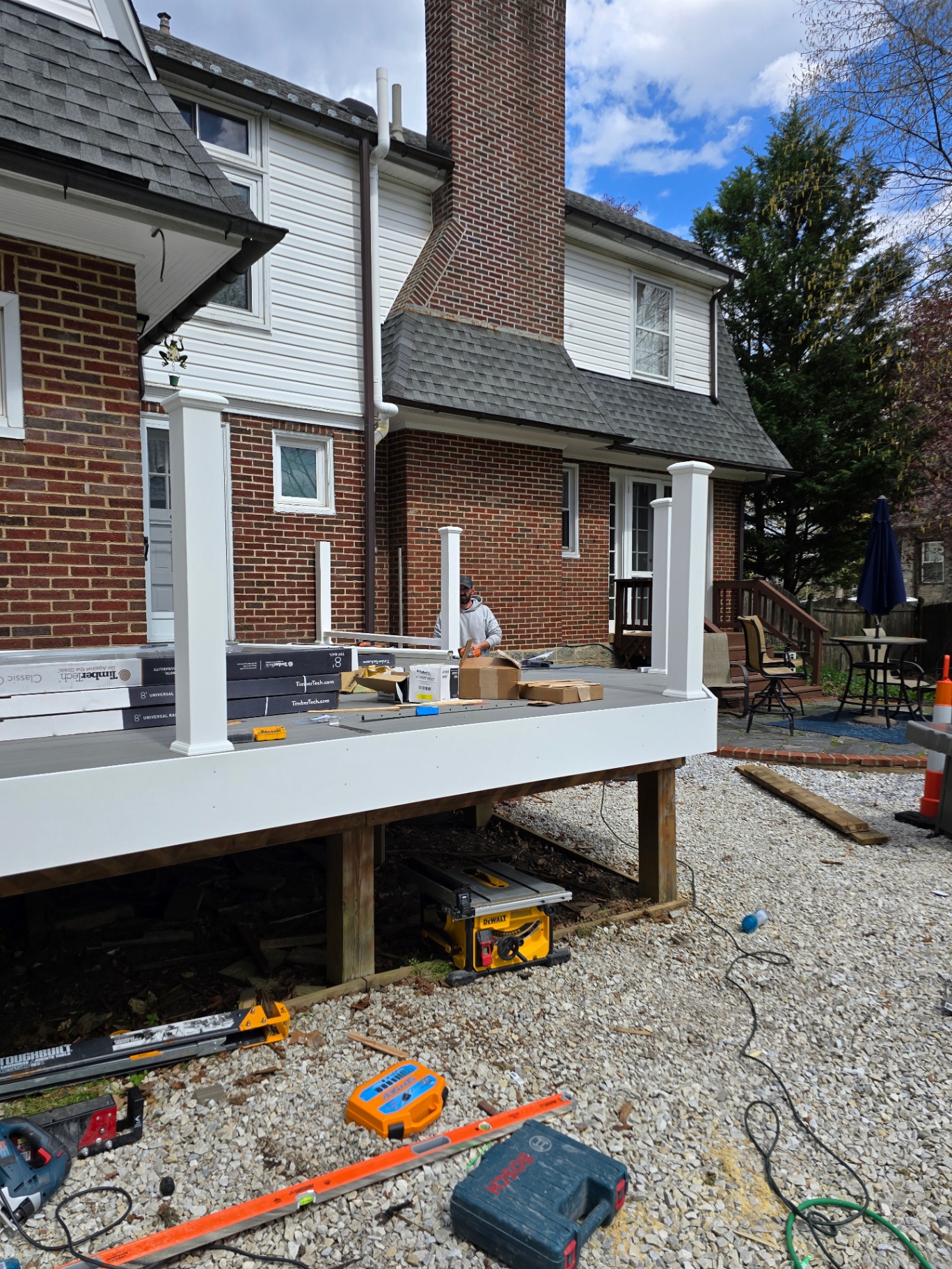 New composite deck installation along the back of a brick home with white posts